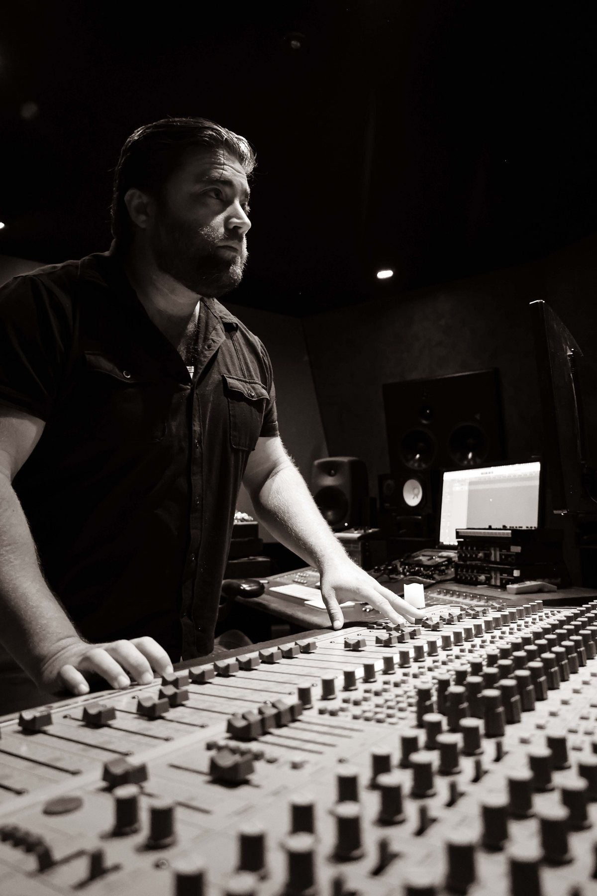 Black-and-white photo of Matt Long at a studio mixing console, hands on the faders