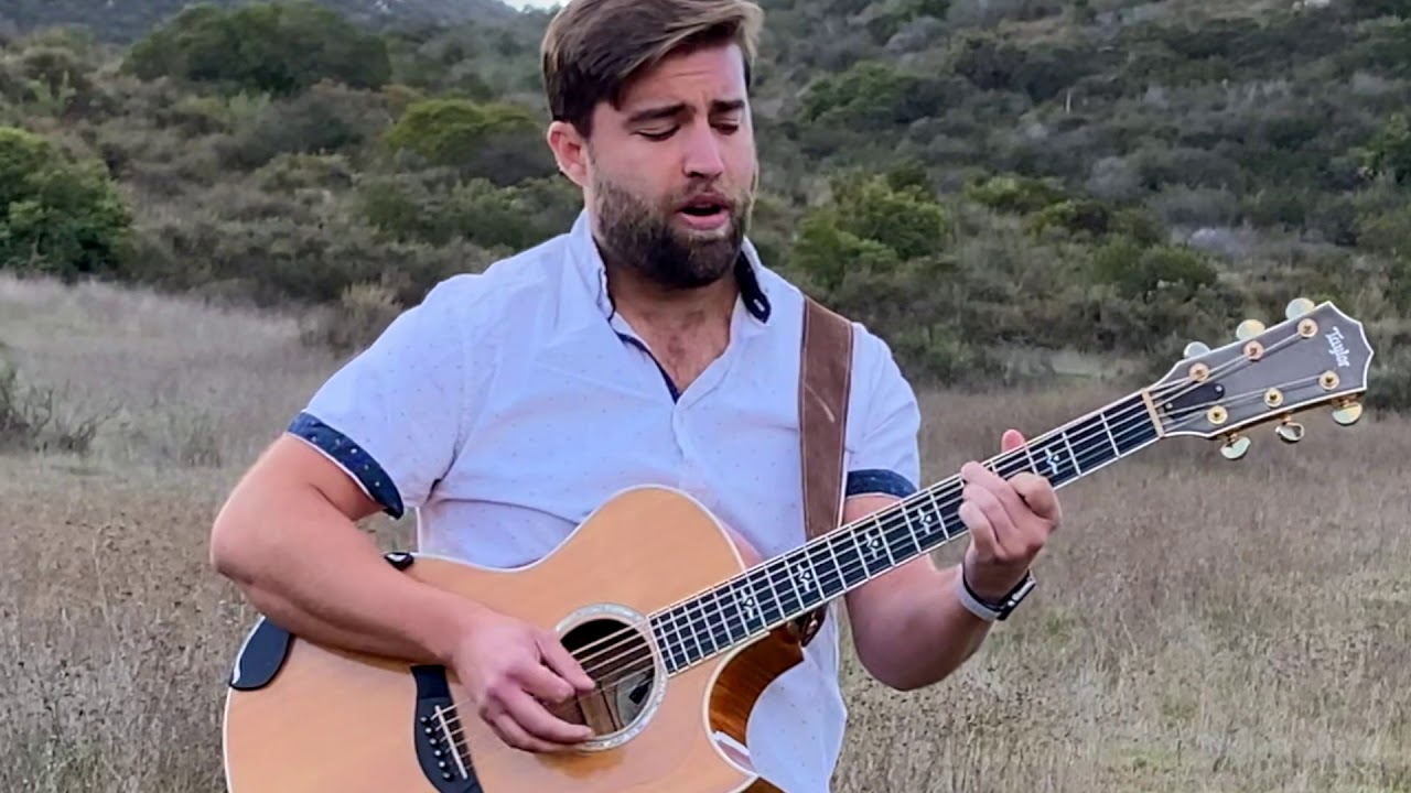 Matt Long in a white shirt playing acoustic guitar and singing outdoors in a grassy field, from his “Together” acoustic video